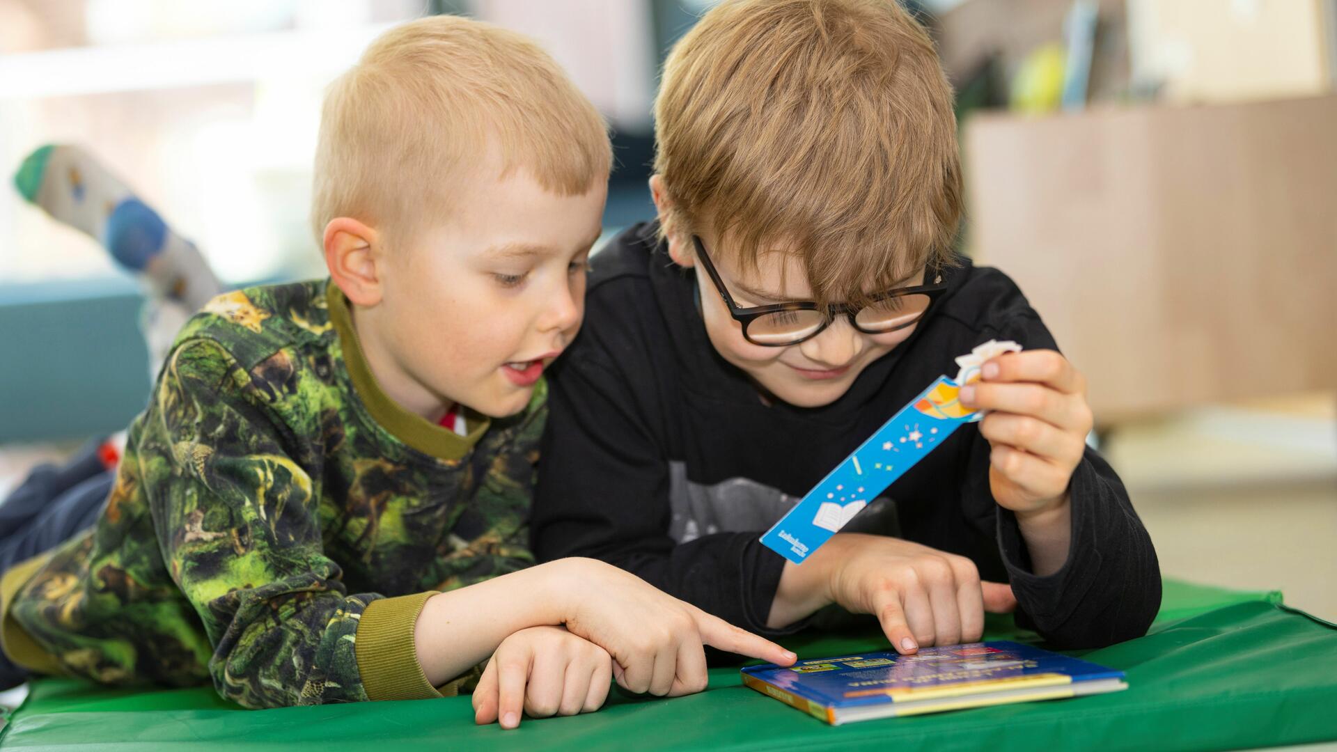 Kaksi lasta lukee kirjaa lattialla maaten. 