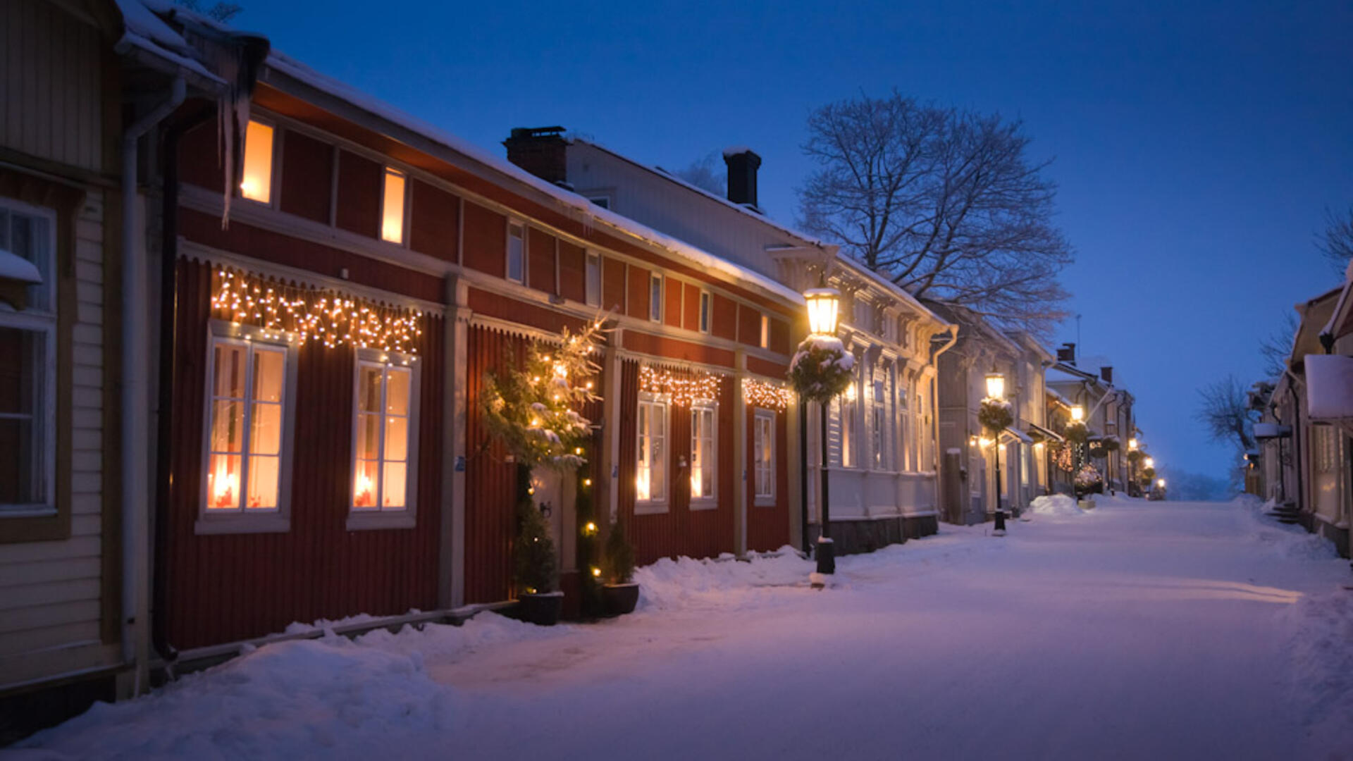 Vanhankaupungin puutalot jouluvaloin koristeltuina lumisena iltana.