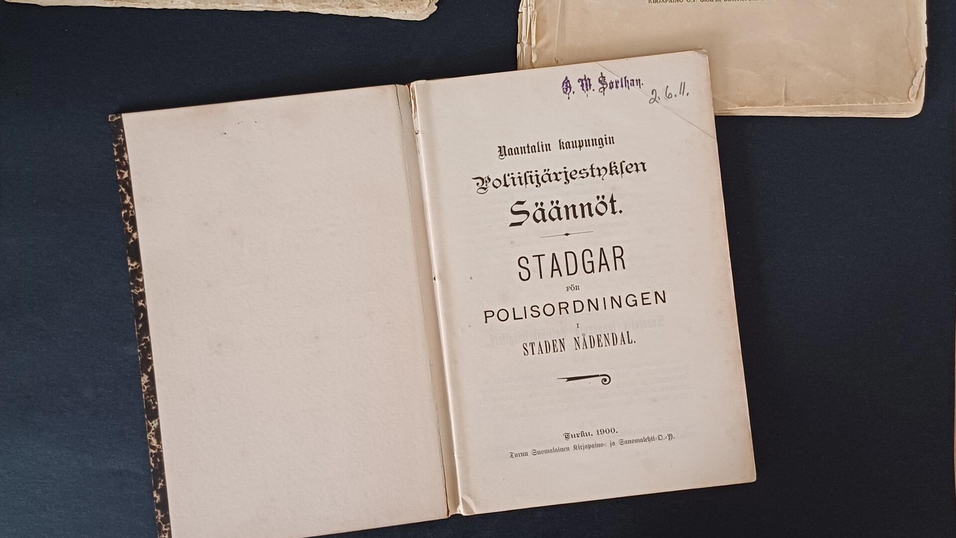 tummalla taustalla avoinna oleva kirja, jossa otsikko "Naantalin kaupungin poliisijärjestyksen säännöt"