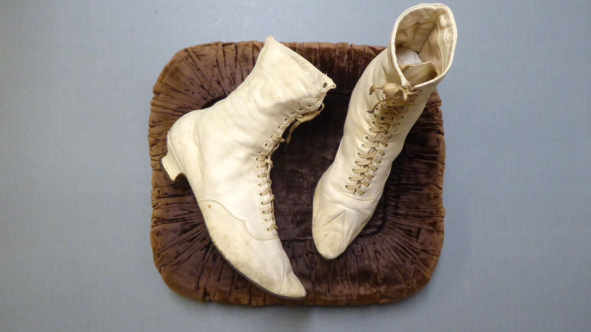 harmaalla taustalla ruskea kangas, jolla valkoiset nyörikengät