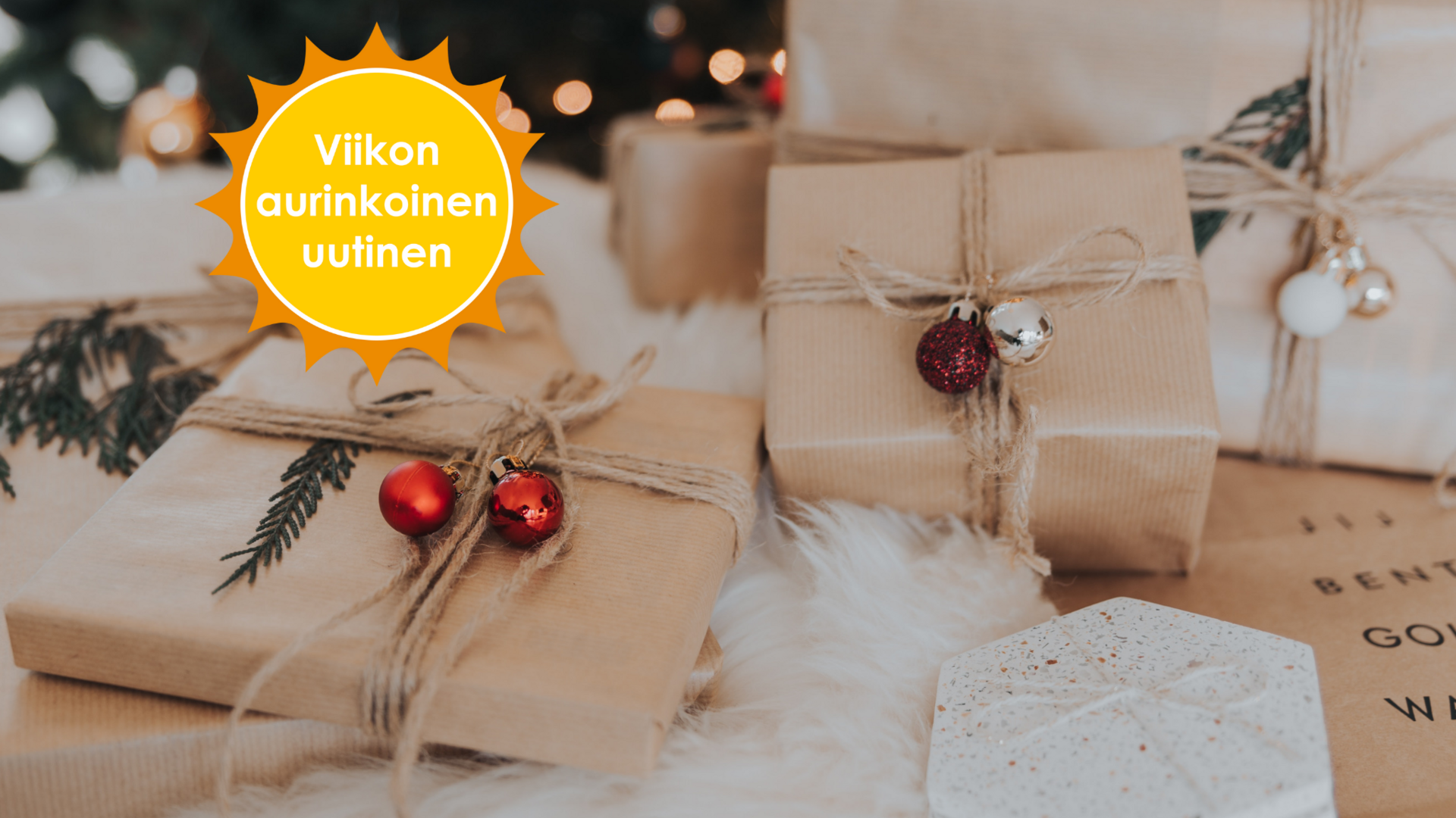 Yksiväriseen ruskeaan paperiin paketoituja, juutinnarulla ja punaisilla joulupalloilla koristeltuja lahjapaketteja kuusen alla. Viikon aurinkoinen uutinen-logo.