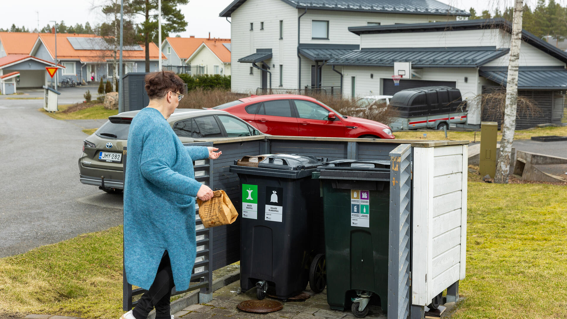 Henkilö kierrättää roskia taloyhtiön roskienkeräyspisteellä.