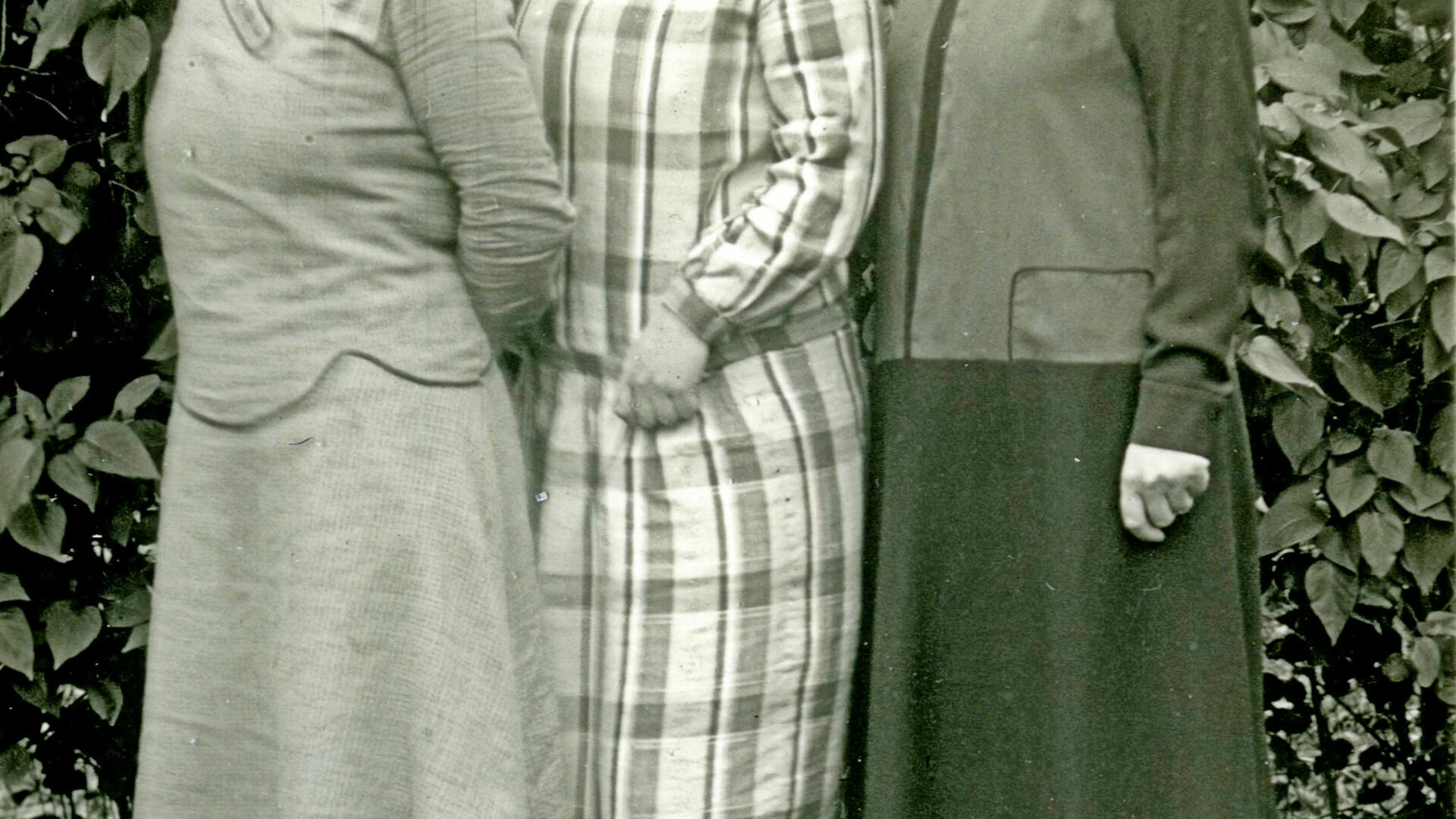 Kolme leninkipukeista naista poseeraa pensaikon edessä