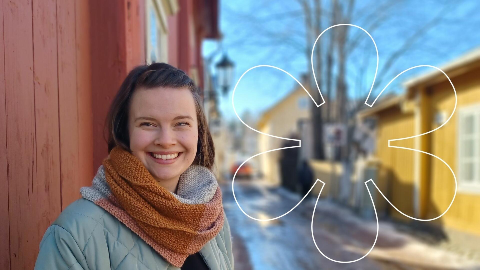 Hymyilevä Heidi Häyry Naantalin Vanhankaupungin puutalojen keskellä, kuvan päällä Onnellinen aurinko -elementti.