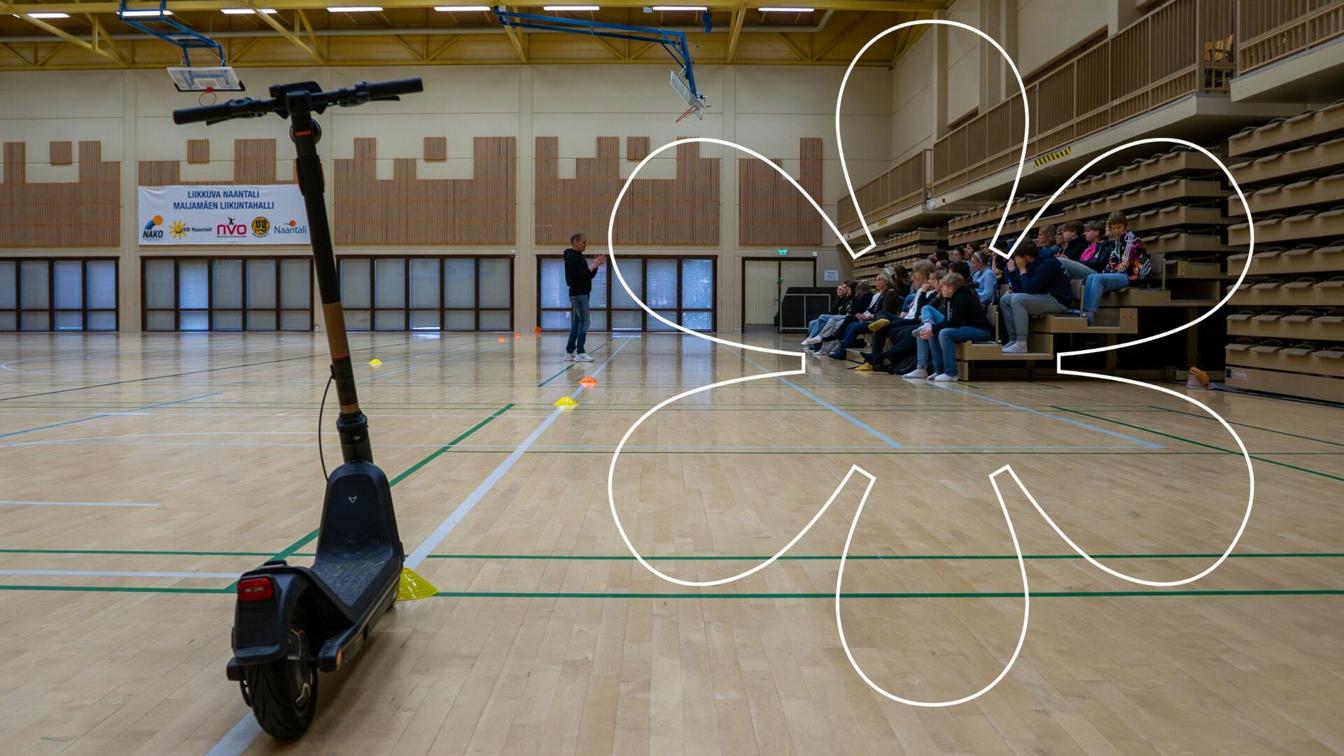 Sähköpotkulauta Maijamäen liikuntahallissa, etäänpänä Sami Kivilä puhumassa nuorelle yleisölle. Kuvassa Onnellinen aurinko -elementti.