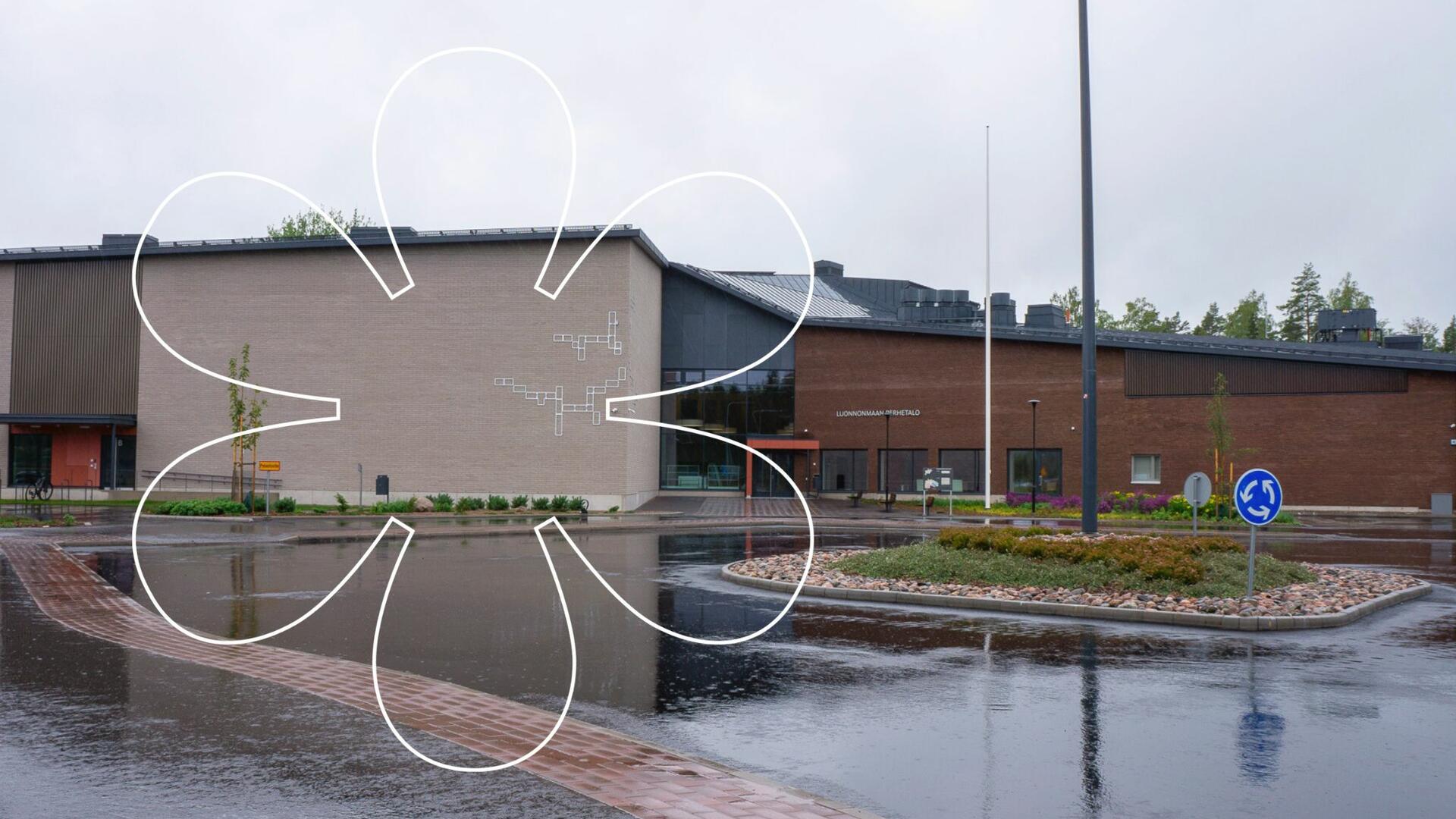 Luonnonmaan perhetalon vaaleanharmaa- ja punatiilinen uudisrakennus, kuvan päällä Onnellinen aurinko -elementti.