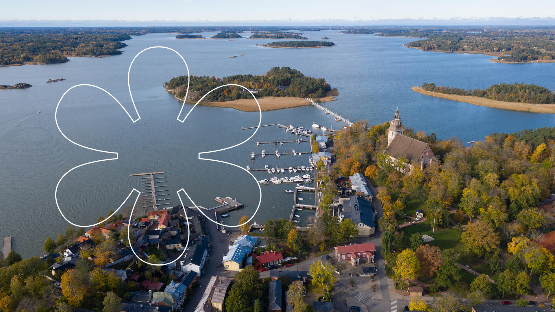 Syksyinen Naantalin Vanhakaupunki kuvattuna ilmasta. Kuvan päällä Onnellinen aurinko -elementti, joka muistuttaa kukkaa tai aurinkoa.