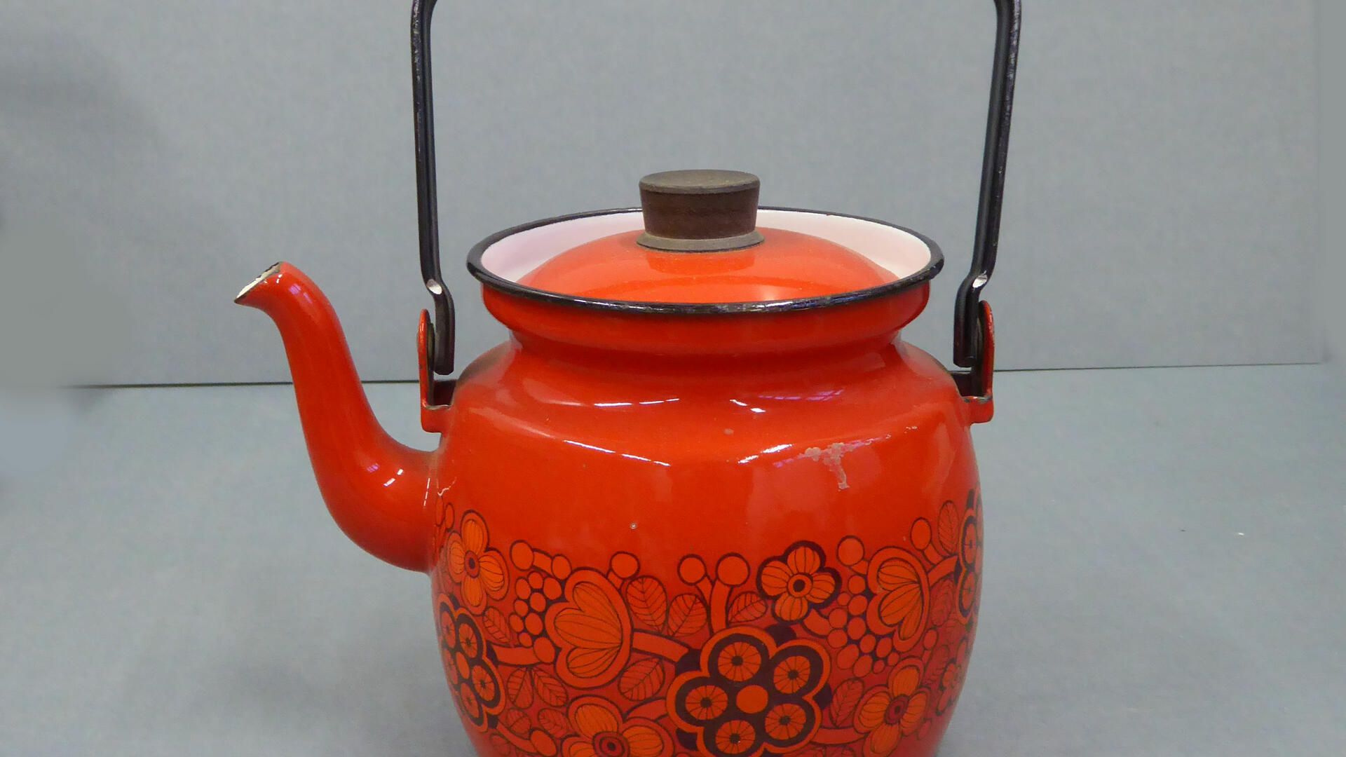 Punainen emalikahvipannu, jota kiertää musta kukkakuvio ja jossa on musta kahva ja kannen nuppi 