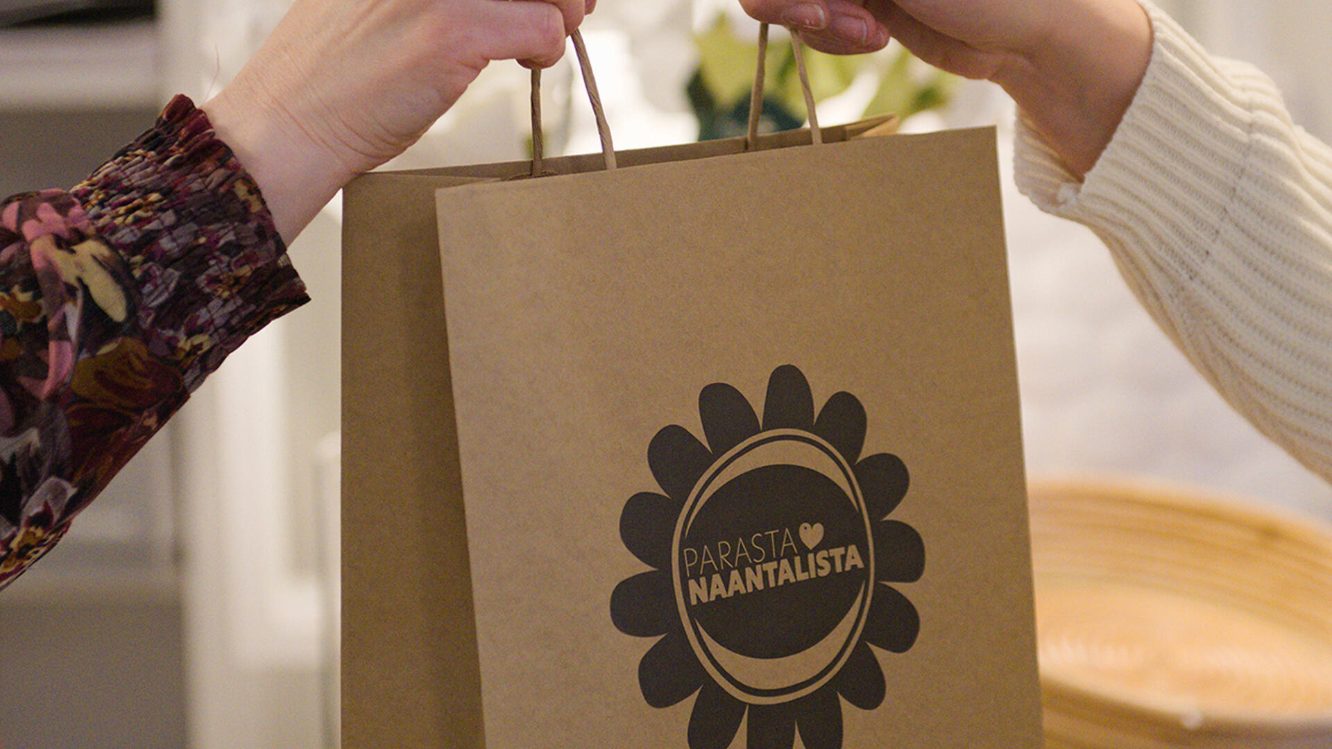 Käsi ojentaa toiselle paperikassin, jossa lukee "Parasta Naantalista"