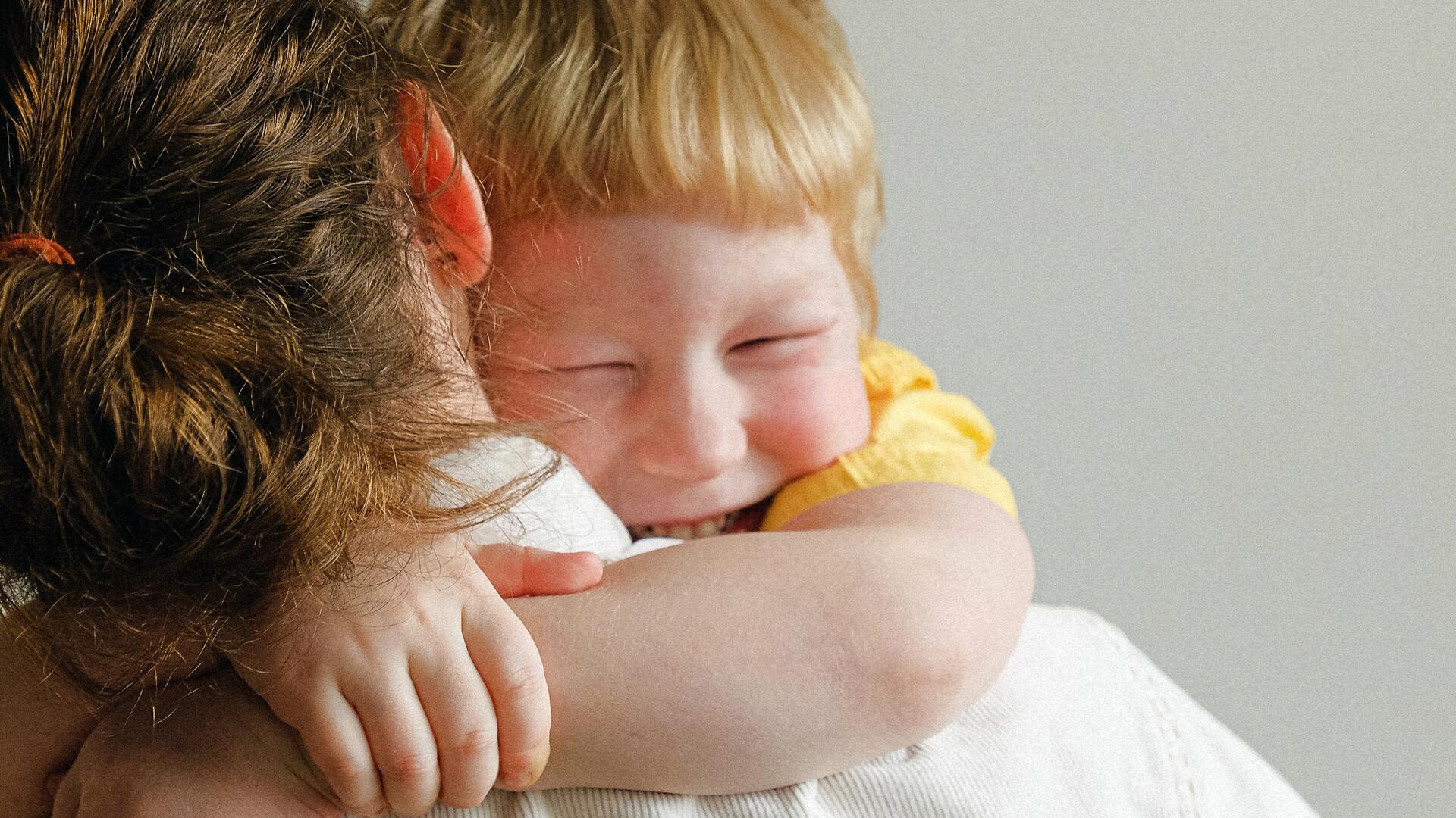 Taapero-ikäinen, naurava poika halaa äitiään.