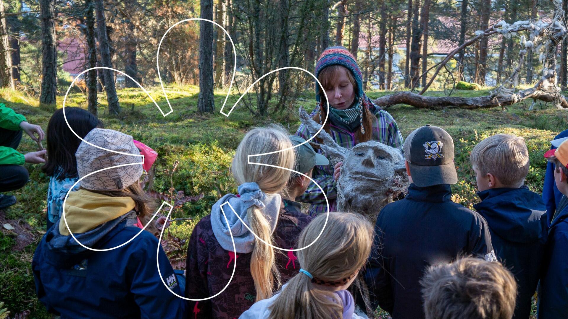 Hanne Lammi esittelee oppilaille luonnonmateriaaleista tehtyä hahmon päätä. Kuvan päällä Onnellinen aurinko -tunnus.