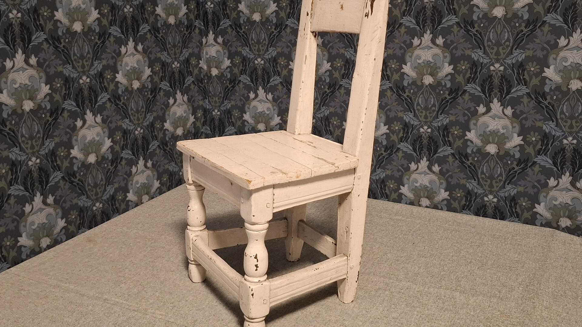 valkoiseksi maalattu puinen tuoli, taustalla sinisävyinen tapetti
