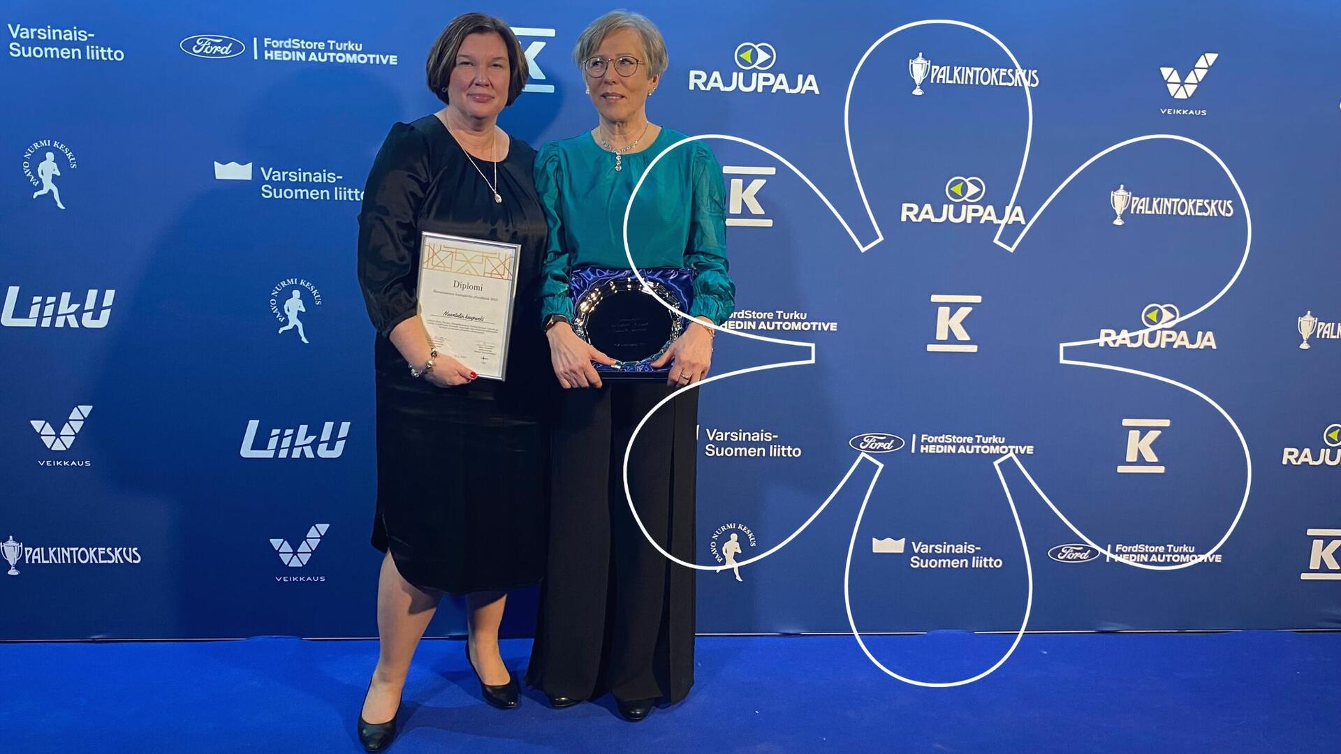 Susanne Nummelin ja Maija Puolakanaho pitelevät palkintodiplomia ja -lautasta. Onnellinen aurinko -elementti.