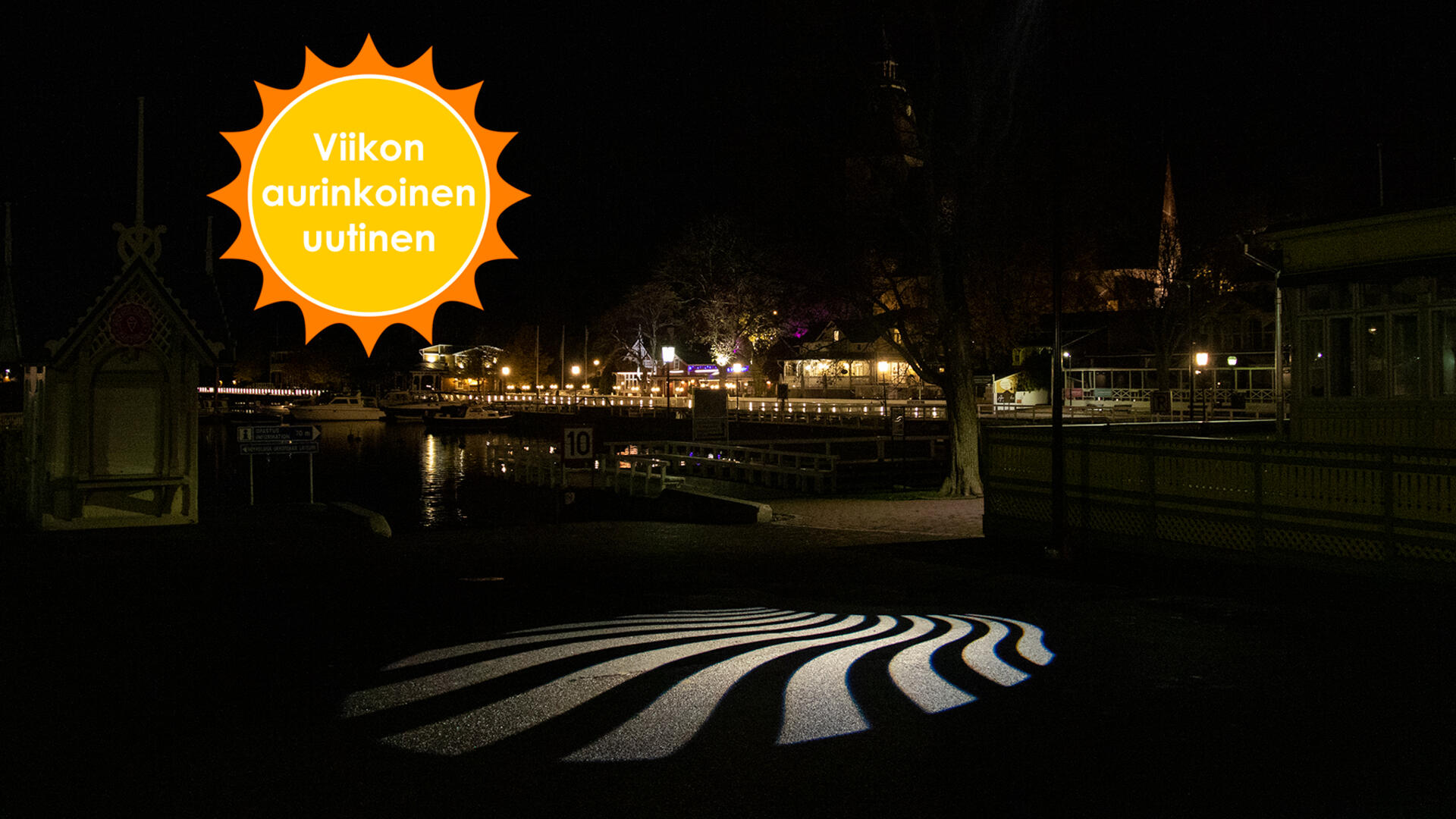 Valo heijastaa aaltoilevat säteet maahan pimeässä Vanhankaupungin rannassa. Taustalla näkyy Naantalin rantaravintolat ja kirkko.Viikon aurinkoinen uutinen.
