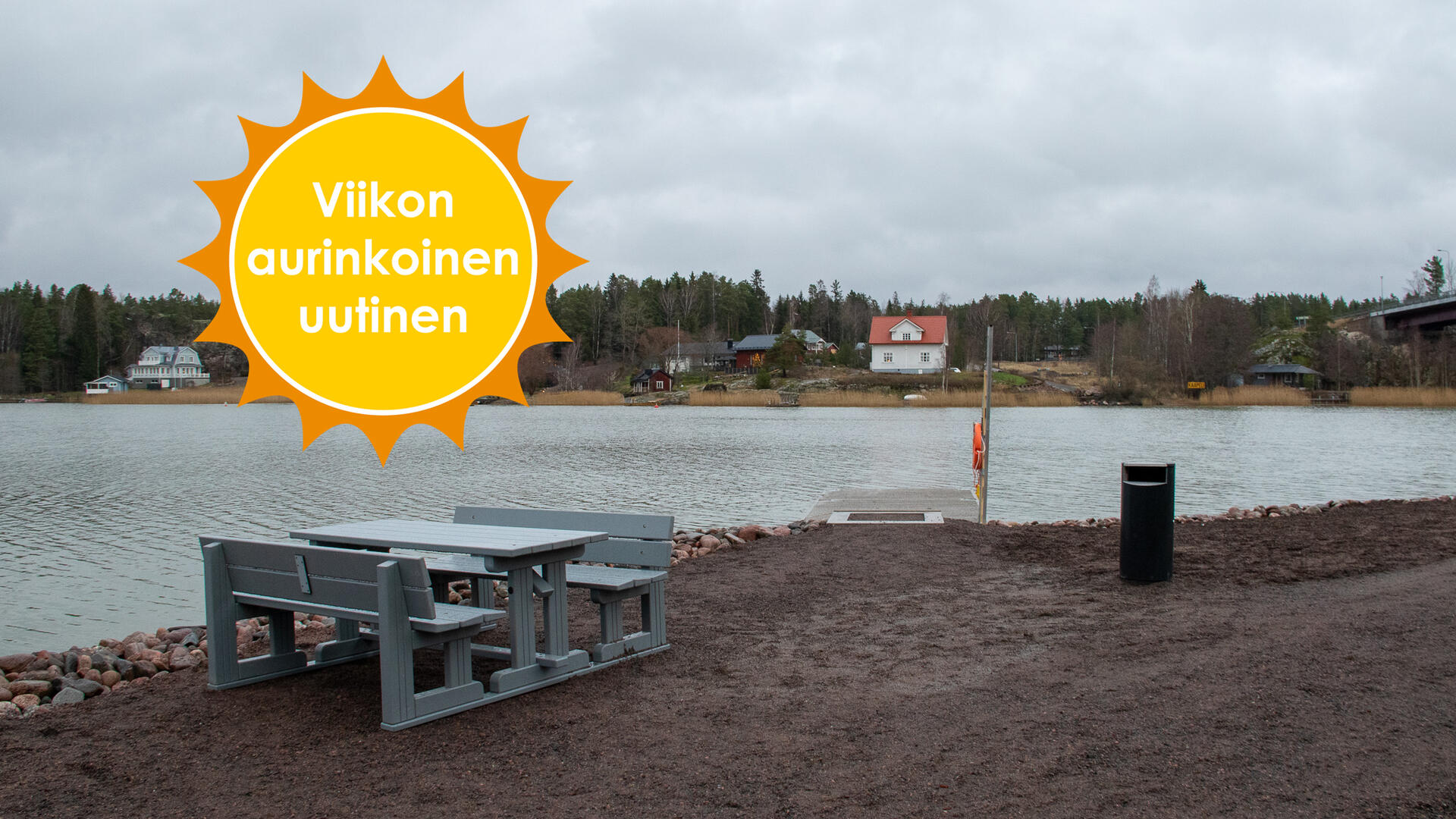 Merimaskun rannassa on harmaa pöytä-penkkiryhmä, roska-astia sekä kalastuslaituri. Viikon aurinkoinen uutinen.