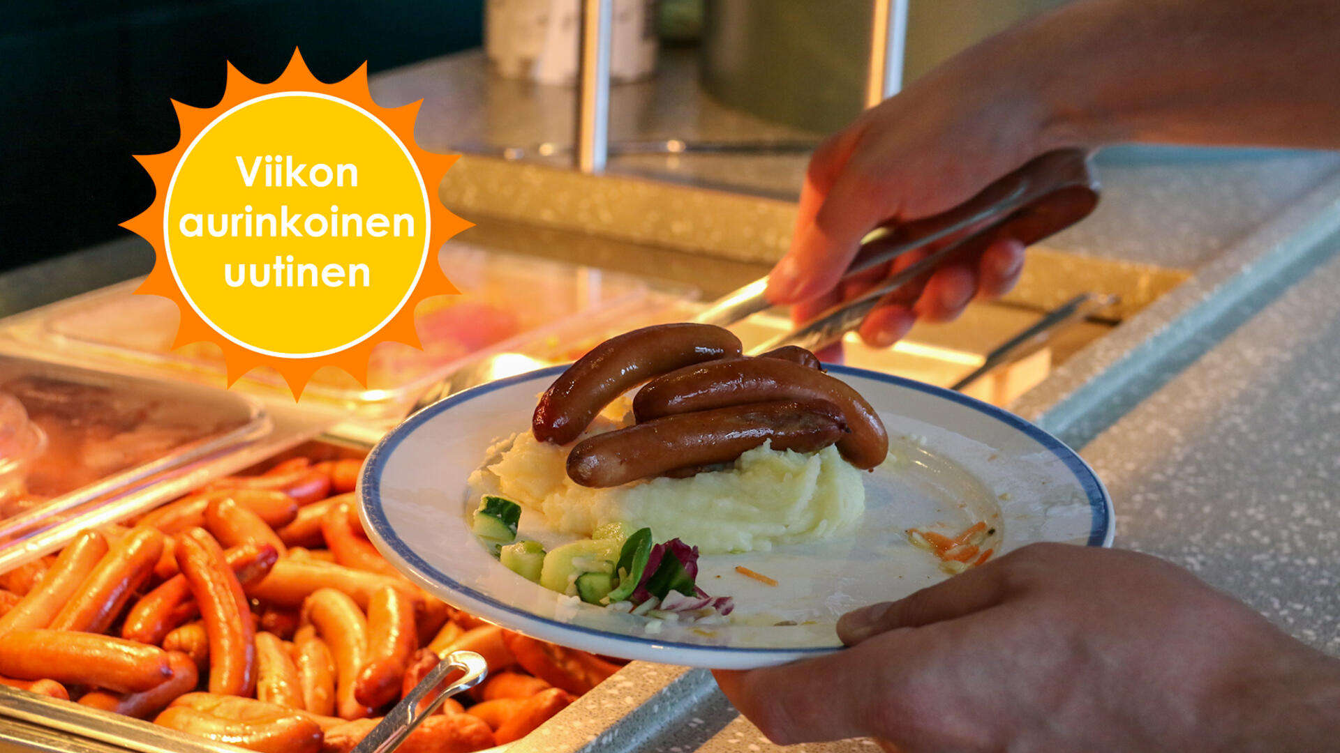 Henkilö ottaa linjastolla lautaselleen nakkeja, kädet ja lautanen, jossa on perunamuusia ja nakkeja, näkyvät kuvassa.