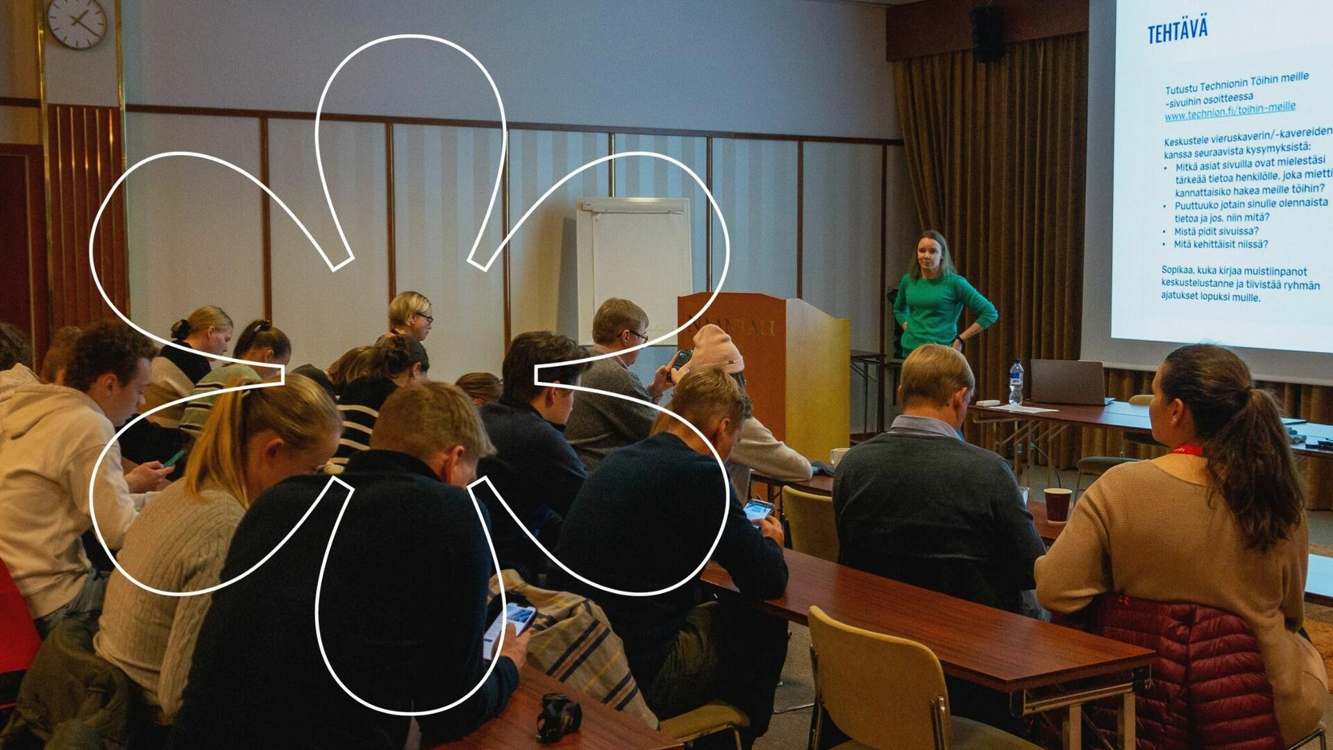 Opiskelijat istuvat salissa, Kati Kekäläinen seisoo edessä. Onnellinen aurinko -elementti.