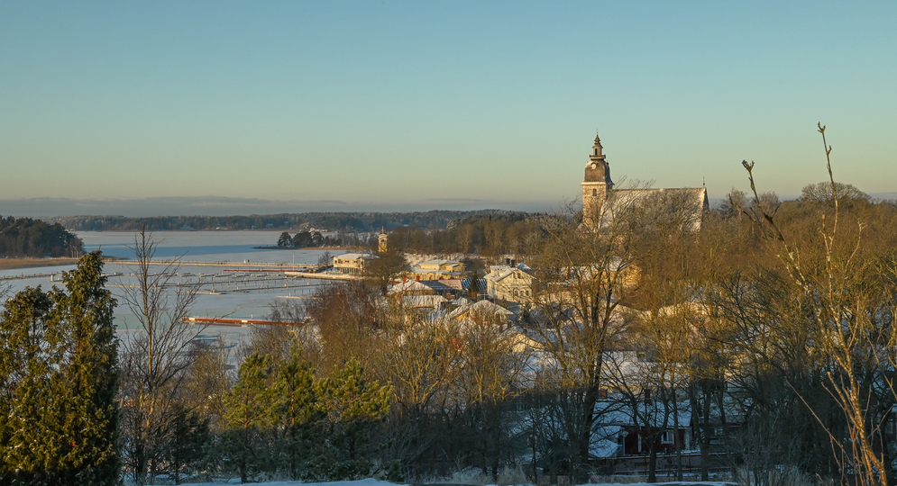 Maisema lumiseen ja aurinkoiseen Naantalin Vanhankaupunkiin ja sen rantaan, keskellä kohoaa luostarikirkon torni.