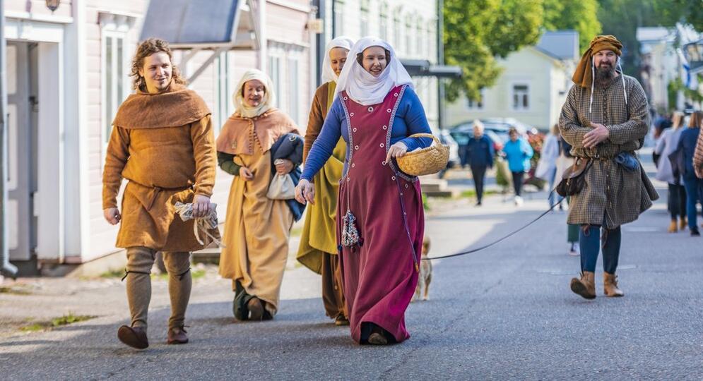 Ryhmä ihmisiä keskiaikaisissa vaatteissa kävelee Vanhankaupungin kadulla.