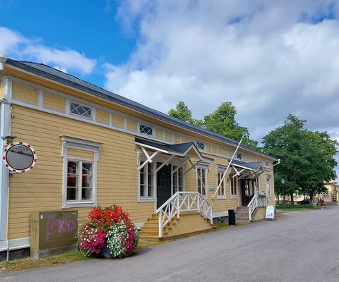 keltaiseksi maalattu puurakennus, edessä kukkaistutus