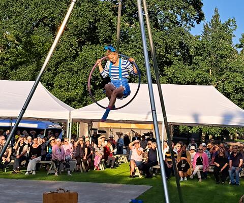 Kirkkopuiston Naantali-päivän juhlassa sirkustaiteilija istuu renkaalla ilmassa.