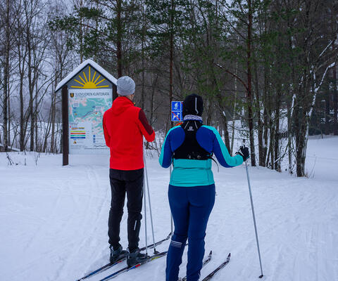 Kaksi hiihtäjää seisoo Suovuoren hiihtolatujen alussa sukset jalassa ja valmistautuu lähtöön.