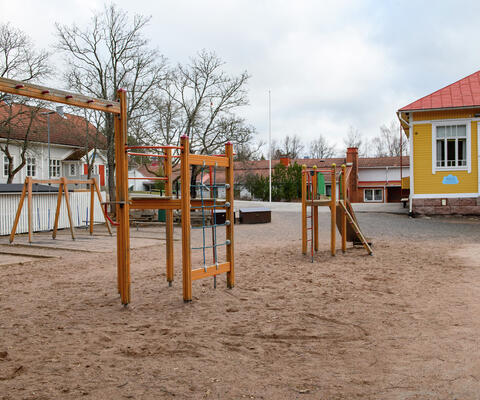 Leikkikentän päässä näkyy Lietsalan koulun keltainen, sininen ja punatiilinen rakennus.