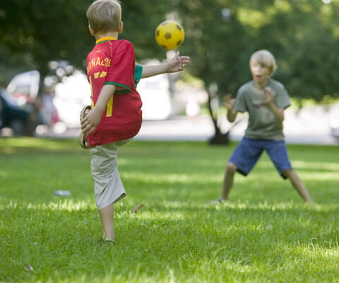 Pojat pelaavat jalkapalloa puistossa