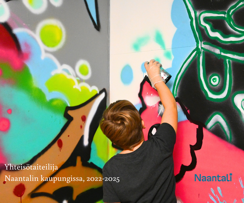 Kuvassa poika maalaa isoa värikästä seinämaalausta. Pojalla on tumma paita ja toisessa kädessä spray-maalipurkki.