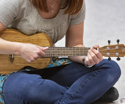 Nainen soittaa ukulelea lattialla istuen