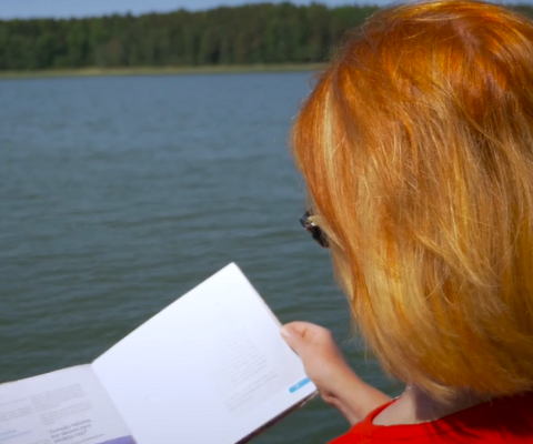 Yrittjä Anne Pentti selaa meren rannassa kirjaa