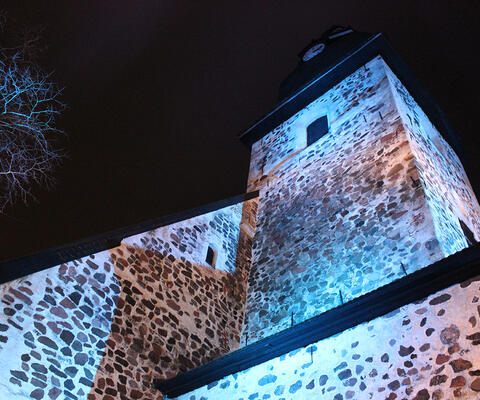 Naantalin kirkon sinisellä valolla valaistu torni kohoaa pimeälle taivaalle.