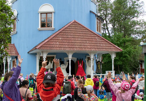 Lapsia jumppaamassa Muumitalon edustalla, jossa Muumipeikko ja pikkumyy neuvovat liikkeitä.