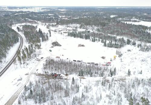 Talvinen maisema ilmasta kuvattuna: vasemmalla kulkee tie, oikealla näkyy paljon metsää ja keskellä raivattua maata, jossa liikkuu työkoneita.