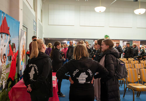 Muumihuppareihin pukeutunutta henkilökuntaa keskustelemassa messuvieraiden kanssa tapahtumassa.