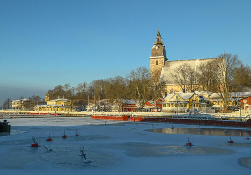 Naantalin vierasvenesatama talvella, rannan kiinteistöjen takana auringonpaisteessa Naantalin kirkko.