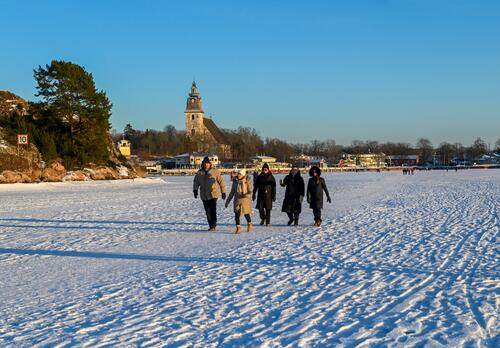 Ihmisiä kävelemässä meren jäillä Naantalissa. Taustalla vierasvenesatama ja kirkko.
