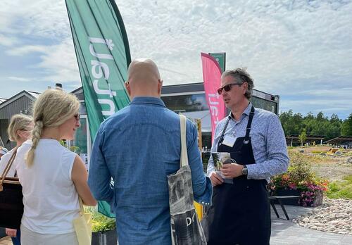 Mustaan essuun pukeutunut mies juttelee ihmisten kanssa, taustalla Naantali-lippuja.