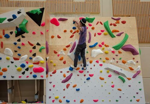 Henkilö boulderointiseinällä, jossa eri värisiä ulokkeita, joista voi ottaa kiinni.