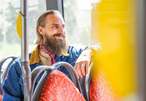 Hymyilevä miesmatkustaja istuu bussissa ja katsoo bussin ikkunasta ulos.
