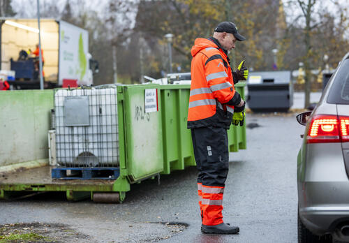 Liikkuvan lajitteluaseman työntekijä kääntyneenä autoon päin, taustalla jätelava.