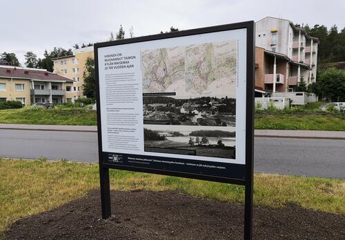 Ulkona metallikehyksessä seisova opastaulu ja taustalla kerrostaloja