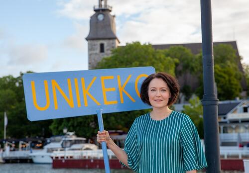 Jenni Haukio raitaan pukeutuneena Naantalin Vanhankaupungin rannassa kädessän Unikeko-kyltti.