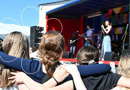 Vaisrockin lavalla Maksuhäiriömerkintä-bändi esiintymässä, etualalla yleisöä. Onnellinen aurinko -elementti.