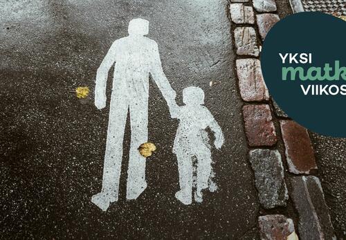 Asfalttiin on maalattu kävelytien merkki, jossa aikuinen ja lapsi kävelevät käsi kädessä.