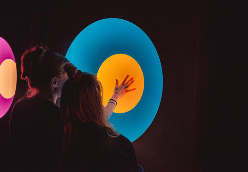 Nainen painaa kätensä värikkään valoteoksen päälle. Kuva Frej Vuori