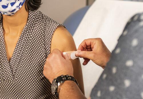 Hoitaja asettaa laastaria rokotettavan käsivarteen.