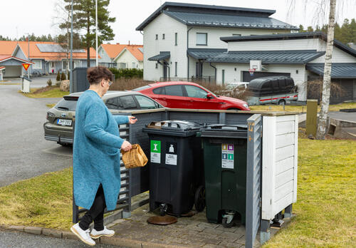 Henkilö kierrättää roskia taloyhtiön roskienkeräyspisteellä.
