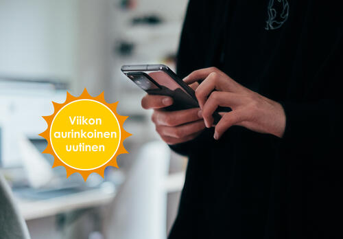 Nainen pitelee kädessään älypuhelinta. Kulmassa Viikon aurinkoinen uutinen -logo.