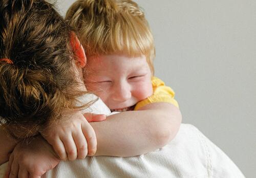 Taapero-ikäinen, naurava poika halaa äitiään.